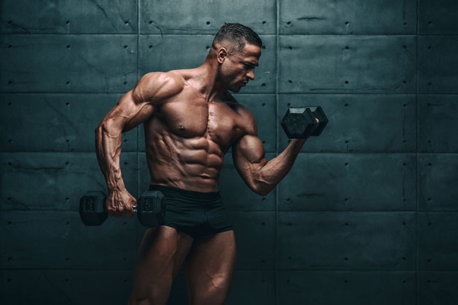 Muscular Men Exercise With Weights. He is performing biceps curls with dumbbels