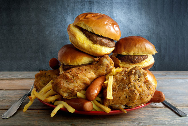 Huge portion of junk food on a plate including burgers, fries, chicken and hot dogs