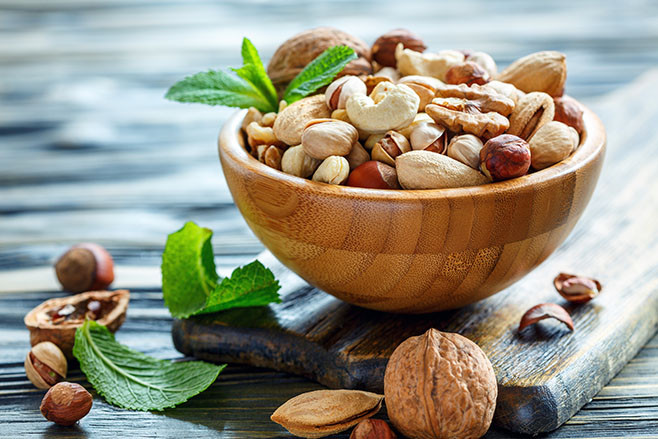 Mixed nuts in a wooden bowl on old table, selective focus.