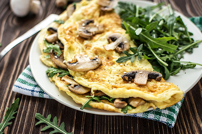 Omelette with mushrooms and arugula on a wooden background