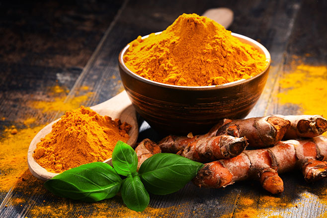 Composition with bowl of turmeric powder on wooden table.