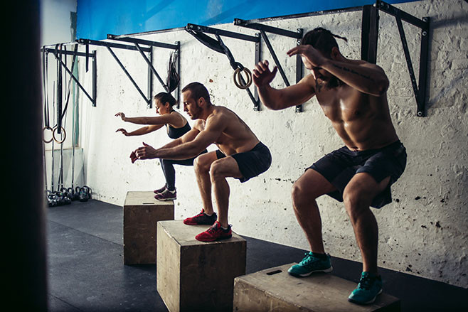 Fit young people doing box jumps as a group in a gym