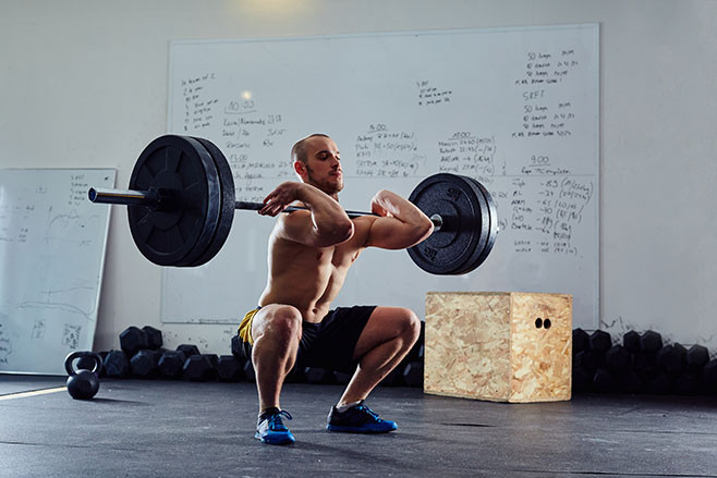 Barbell front squat exercise - athletic man during intense workout at the gym