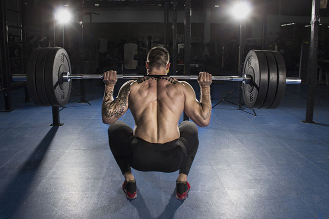 Attractive muscular shirtless bodybuilder doing heavy squat exercise in modern fitness center.Functional training.Back view.