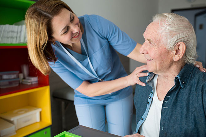 Happy caretaker assisting senior man. Friendly nurse supporting old man with Parkinson's Disease