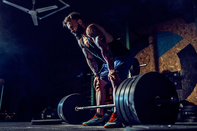 Muscular fitness man preparing to deadlift a barbell over his head in modern fitness center. Functional training. Snatch exercise