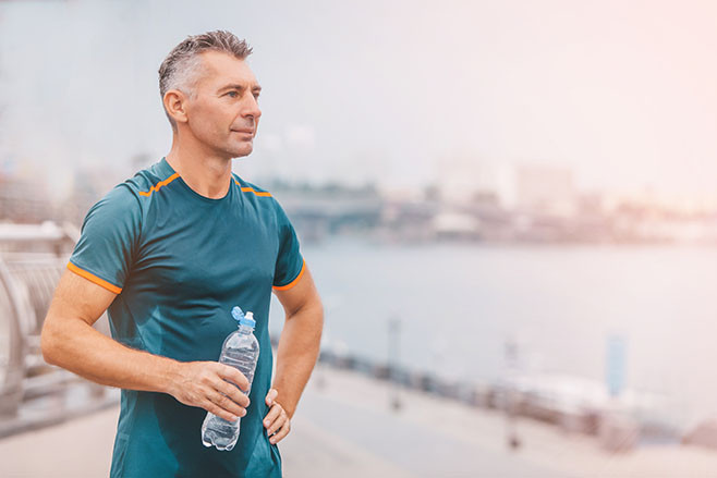 Portrait of healthy athletic middle aged man with fit body holding bottle of refreshing water, resting after workout or running. middle aged male with a drink after outdoor training.