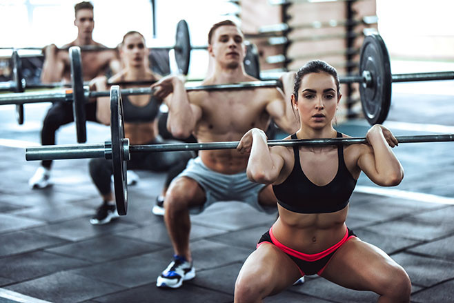 Group of sporty muscular people are working out in gym. Cross fit training. Handsome shirtless men and attractive women are doing exercises with barbells. Weightlifting.