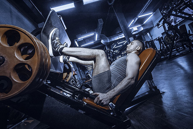 Man Using A Press Machine In A Fitness Club. Toned image. Man doing an exercise on its legs in the simulator. side view