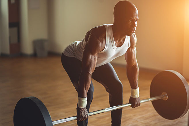 Young shirtless man doing deadlift exercise at gym. Screaming for motivation