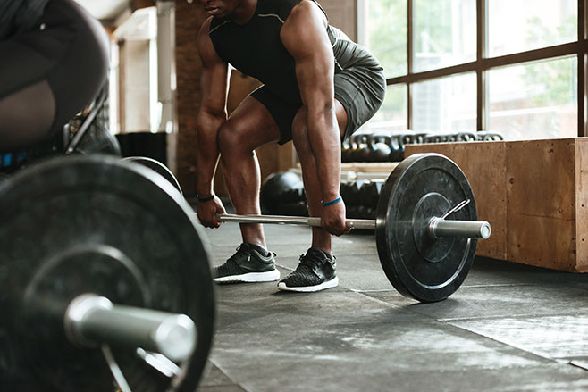 Cropped image of a young african sportsman lifting a barbell at the gym