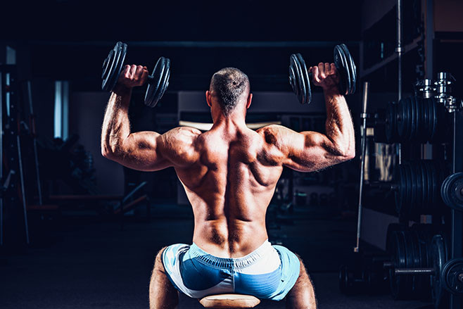 Muscular man training his shoulders with dumbbells in gym