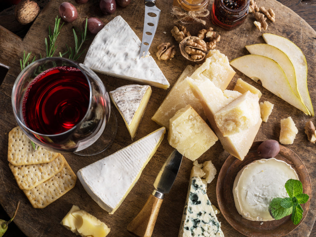 Cheese platter with organic cheeses, fruits, nuts and wine on wooden background. Top view. Tasty cheese starter.