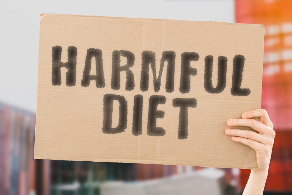 The phrase " Harmful diet " on a banner in men's hand with blurred background. Healthcare. Dangerous. Nutrition. Life. Essential. Hazardous